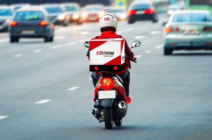 Um homem sentado à secretária no computador e do lado direito um distribuidor dos CTT